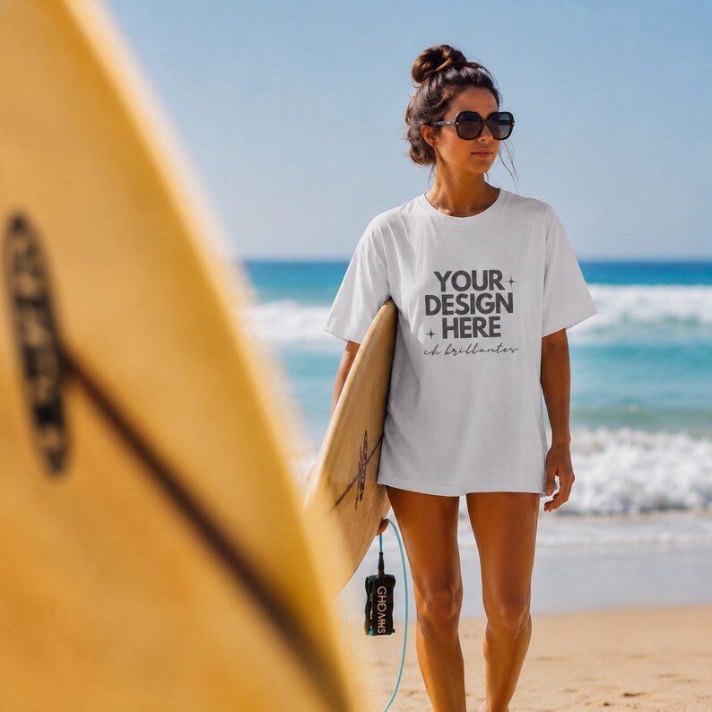 May include: A white short-sleeved t-shirt featuring the black text "YOUR DESIGN HERE" with small star icons and the cursive script "oh brillanter" printed on the front. The shirt is worn with dark-rimmed sunglasses and a hair bun.