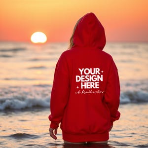 Puede incluir: Una sudadera con capucha roja con una impresión blanca que dice "YOUR DESIGN HERE" y "ch brillantes". La sudadera con capucha la lleva puesta una persona de pie en el agua de la playa.