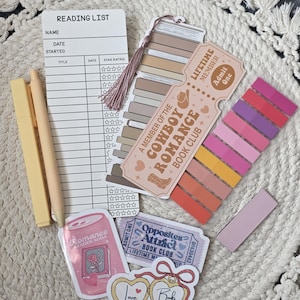 May include: A collection of stationery items for book lovers, including a reading list, bookmarks, stickers, and pens. The items feature a color palette of beige, pink, and peach. The stickers have the text "Romance Reader Soda", "Opposites Attract Book Club", and "Love Books".