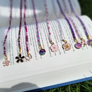 May include: A set of eight colorful beaded eyeglass chains with different charms. The charms include a butterfly, a flower, a dragonfly, a daisy, a cherry blossom, and a galaxy design.