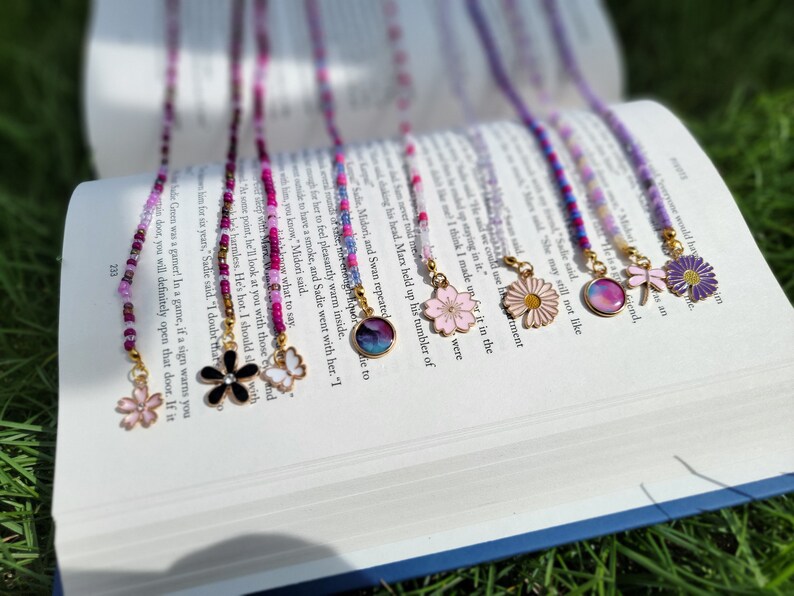 May include: A set of eight colorful beaded eyeglass chains with different charms. The charms include a butterfly, a flower, a dragonfly, a daisy, a cherry blossom, and a galaxy design.