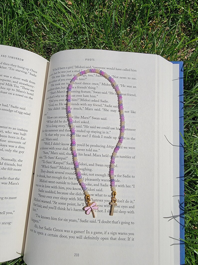 May include: A close-up of a book with a purple, white, and yellow beaded necklace with butterfly charms. The book is open to a page with the text "PIVOTS" and the text "I doubt that's going to happen."