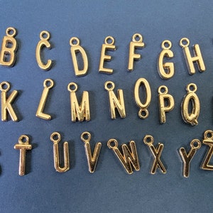 May include: Gold-coloured metal alphabet letter charms. Each letter is separate and has a loop for attaching to a necklace, bracelet, or other jewellery.
