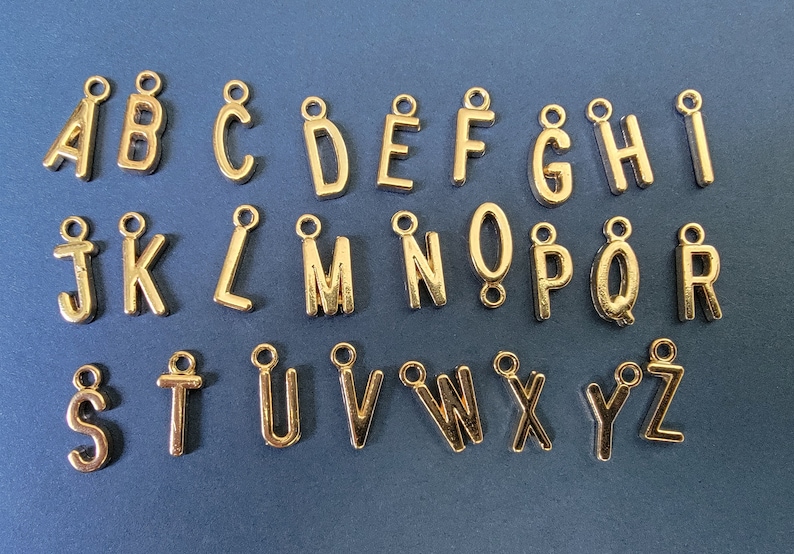 May include: Gold-coloured metal alphabet letter charms. Each letter is separate and has a loop for attaching to a necklace, bracelet, or other jewellery.