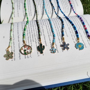 May include: A collection of beaded reading glasses chains with various charms, including a mermaid, a cactus, a flower, and a daisy. The chains are made with different coloured beads, including green, blue, and white.
