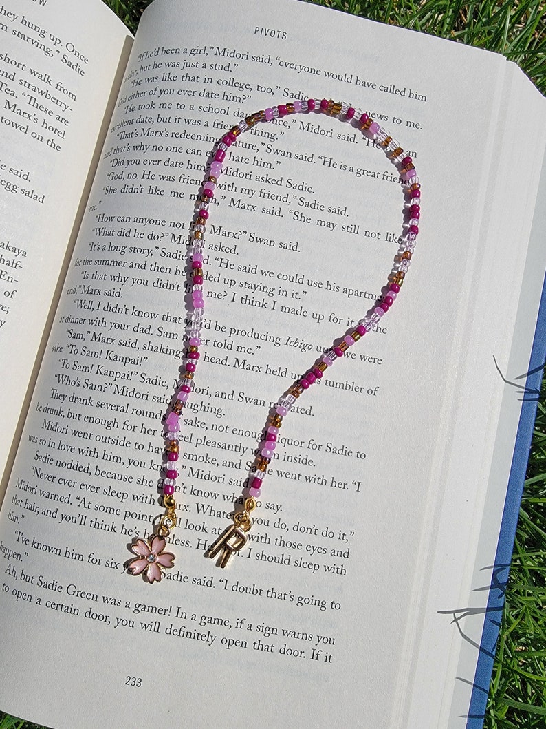 May include: A close-up of a book with a pink and gold beaded bracelet on top of it. The book is open to a page with the word "PIVOTS" at the top. The bracelet has a small pink flower charm attached to it.