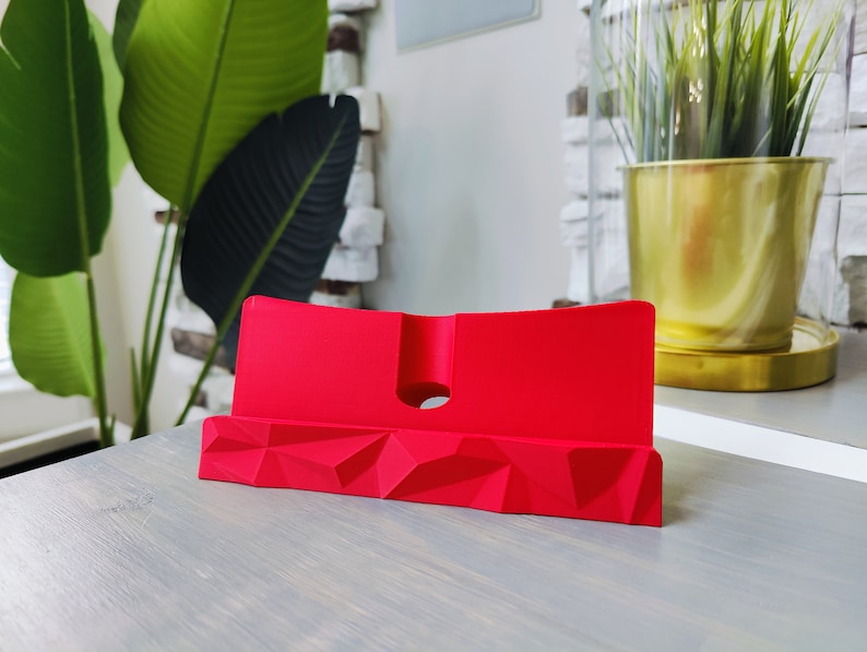 K&ouml;nnte beinhalten: Ein roter Telefonst&auml;nder mit geometrischem Design. Der St&auml;nder ist aus einem glatten, kunststoffartigen Material gefertigt.