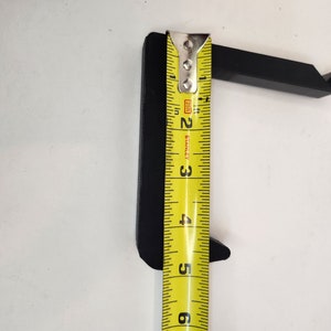 May include: A black plastic hook with a measurement of 5 inches, measured with a yellow tape measure.