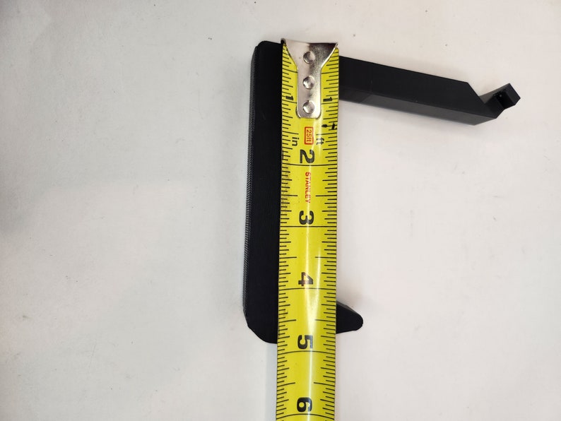 May include: A black plastic hook with a measurement of 5 inches, measured with a yellow tape measure.