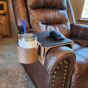 May include: A brown leather recliner with a wooden armrest tray. The tray has a cup holder, a pen holder, and a mouse pad. A black wireless mouse is on the mouse pad.