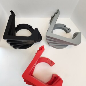 May include: Three 3D printed stands in black, gray, and red. Each stand is made of multiple layers and has a circular opening in the center.