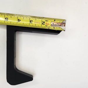 May include: Black plastic corner bracket with a measurement of 2 inches. The bracket is designed to be used for joining two pieces of wood or other materials at a 90-degree angle.