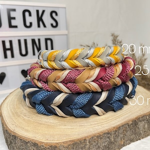 May include: Three braided leather dog collars in different colors and widths: 20 mm, 25 mm, and 30 mm. The collars are stacked on top of each other on a wooden surface.