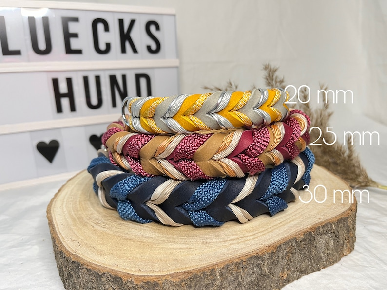 May include: Three braided leather dog collars in different colors and widths: 20 mm, 25 mm, and 30 mm. The collars are stacked on top of each other on a wooden surface.