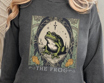 May include: A dark gray sweatshirt with a graphic print of a green frog wearing a crown and surrounded by stars and foliage. The text "THE FROG" is printed below the frog.
