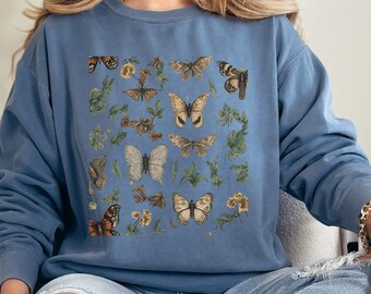 May include: A blue sweatshirt with a vintage-style print of butterflies and flowers. The sweatshirt has a crew neck and long sleeves.