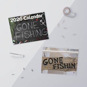 Puede incluir: Dos calendarios de espiral de 2026. Uno muestra "GONE FISHING" en una pizarra con aparejos de pesca. El otro calendario muestra un letrero de madera que dice "GONE FISHIN'".