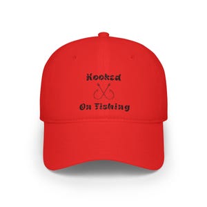 Può includere: Cappellino da baseball rosso con testo ricamato nero che recita "hooked on fishing" e due ami da pesca incrociati.