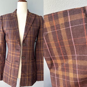 May include: A brown plaid blazer with a classic design. The blazer has a two-button closure, notched lapels, and two front pockets. The plaid pattern includes shades of brown, orange, and white. The blazer is displayed on a mannequin.