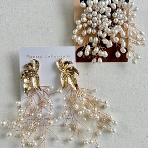 Puede incluir: Pendientes dorados con forma de hoja con perlas de imitación colgantes y un accesorio para el cabello a juego. Los pendientes presentan un diseño de hoja dorada con cristales transparentes y delicados hilos de perlas. El accesorio para el cabello es un racimo de perlas sobre alambre dorado.