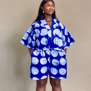 Może przedstawiać: Dwuczęściowy strój z niebiesko-białym wzorem. Zestaw składa się z bluzki z krótkim rękawem i pasujących szortów. Tkanina ma powtarzający się wzór dużych, nieregularnych białych kół na ciemnoniebieskim tle. Strój ma luźny krój.
