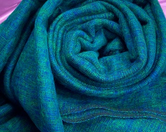 Pode incluir: Uma echarpe macia, com padrão azul e verde, feita de lã. A echarpe está enrolada e as bordas são visíveis.