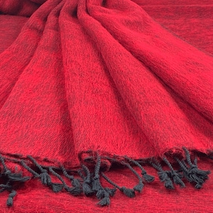 May include: A red and black wool shawl with black fringe. The shawl is folded and draped over a surface.