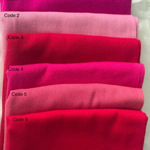 May include: Six folded fabric swatches in varying shades of pink and red. The colours include deep magenta, light pink, and bright red. Each swatch is labelled with a code: Code 1, Code 2, Code 3, Code 4, Code 5, and Code 6.