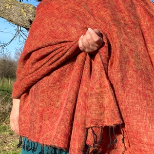 Może przedstawiać: Duży, rdzawo-brązowy szal z czarnym frędzlem. Szal jest wykonany z miękkiego, puszystego materiału i jest zarzucony na ramiona osoby.