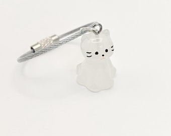 May include: A silver cable keychain with a white cat charm. The cat has black eyes and whiskers and a pink nose.