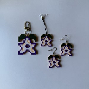 May include: Three purple and gold star-shaped charms with green leaves. The charms are attached to keychains and earrings.