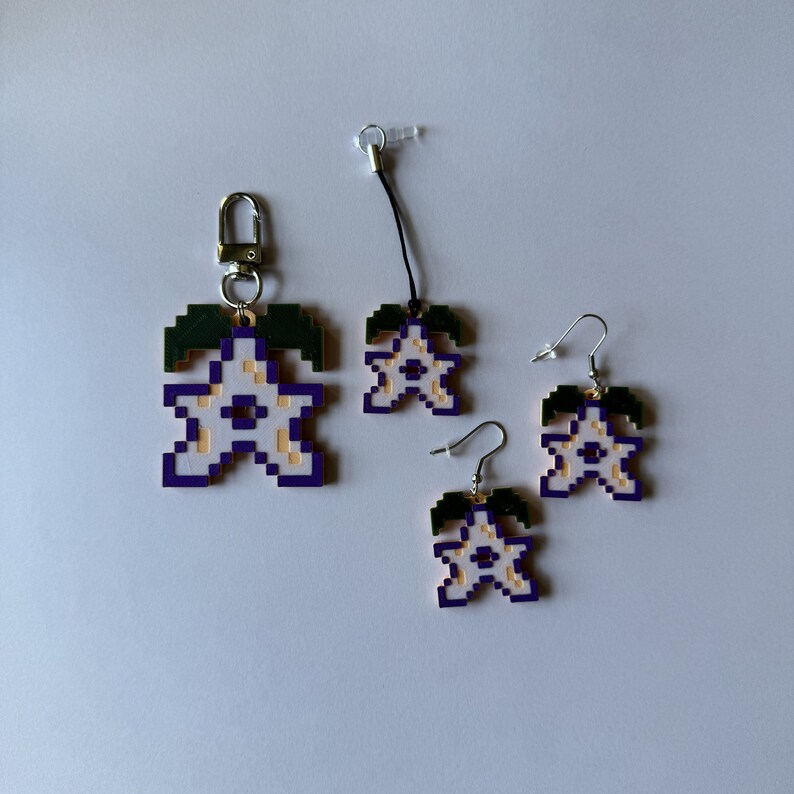 May include: Three purple and gold star-shaped charms with green leaves. The charms are attached to keychains and earrings.