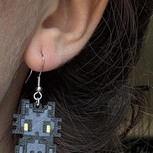 Puede incluir: Pendientes de gato pixelados grises con ojos amarillos. Los pendientes tienen un gancho plateado. Un accesorio &uacute;nico para los amantes de los gatos. Una adici&oacute;n divertida y peculiar a cualquier atuendo.