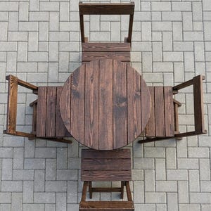 Könnte beinhalten: Ein dunkelbraunes Esszimmerset aus Holz, bestehend aus einem runden Tisch und vier passenden Stühlen, die in einem Kreuzmuster angeordnet sind. Die Möbel weisen eine sichtbare Holzmaserung und ein Latten-Design an Tischplatte und Sitzen auf.