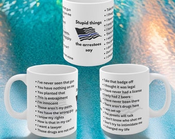May include: Three white coffee mugs with black text listing common phrases said by people who have been arrested. The mugs feature a blue and white American flag with a thin blue line.