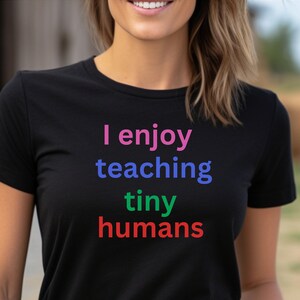 May include: A black t-shirt with the text "I enjoy teaching tiny humans" in pink, blue, green, and red.