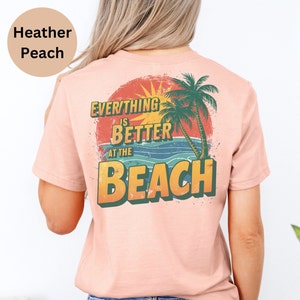 May include: A heather peach t-shirt with a vintage-style graphic that says "Everything is better at the beach". The graphic features a sunset, palm trees, and ocean waves.