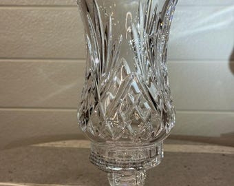 May include: A clear crystal vase with a flared top and intricate cut glass patterns. The vase features a diamond and leaf design, sitting on a pedestal base. The vase is approximately 10 inches tall.