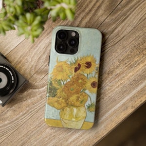 May include: A phone case with a painting of sunflowers in a vase. The case is white with a light blue background. The sunflowers are yellow with brown centers and green leaves. The vase is brown and white.
