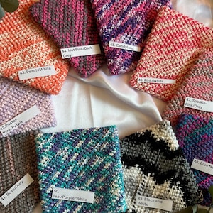 May include: A collection of 10 crocheted squares in various color combinations, including pink, purple, teal, grey, white, and black. Each square has a label with a number and a color description, such as "Pastel-Pink/Purple" and "Hot Pink/Dark Grey".