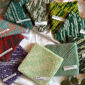 May include: Ten different colored knitted dishcloths with white accents. Each dishcloth has a number and a description of the color combination. The dishcloths are arranged in a circle on a white surface.