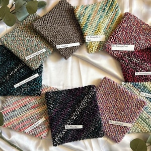 May include: Ten different colors of knitted fabric swatches, each with a unique speckled pattern and a number and name tag. The swatches are arranged in a circle on a white satin surface.