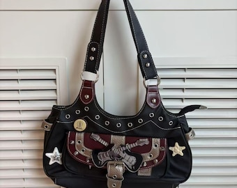 Può includere: Borsa a tracolla nera con finiture argentate, borchie e un'applicazione a forma di chitarra. La borsa presenta un manico superiore, una fibbia decorativa e abbellimenti a forma di stella. La borsa è larga circa 30 cm.