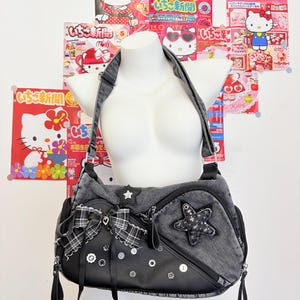 May include: A dark gray denim and black faux leather shoulder bag featuring a large black and white plaid ribbon bow, a star-shaped patch with silver studs, a small star accent, and multiple circular buttons attached to the front panel.