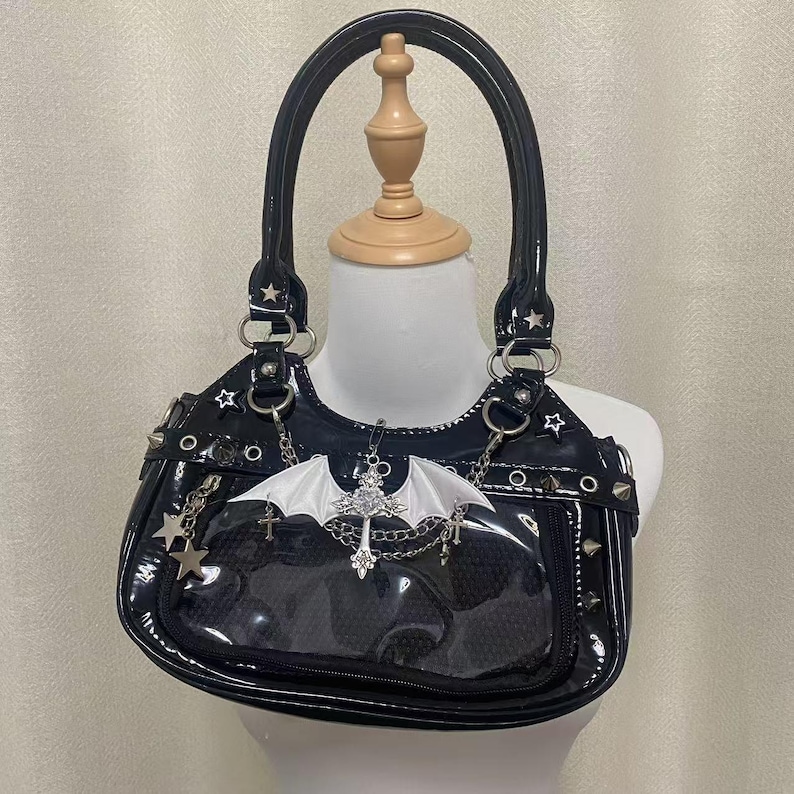 May include: A black patent leather handbag with silver hardware and a bat charm. The bag has a clear plastic panel on the front and a zip closure.