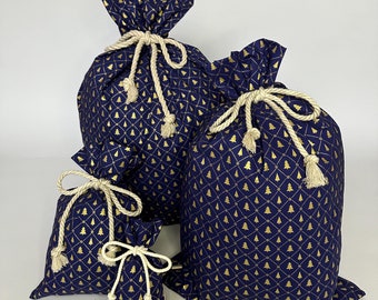 May include: Three blue fabric gift bags with gold Christmas tree patterns and white drawstrings. The bags are arranged in size order from largest to smallest.