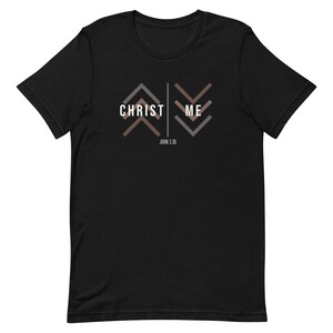Puede incluir: Camiseta negra con las palabras "CHRIST ME" en blanco, con diseños geométricos de flechas en marrón y gris. El texto "JOHN 3:30" está debajo. Diseño sencillo y moderno.
