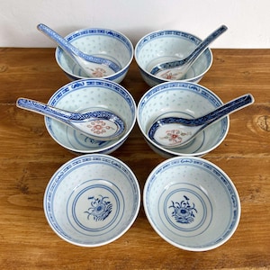 May include: A set of six white and blue porcelain bowls and spoons on a wooden surface. The bowls feature a blue floral design and a pierced pattern. The spoons have blue handles and floral designs. A classic Asian-inspired tableware set.