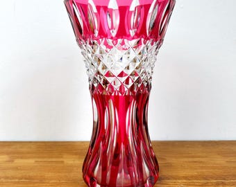 Puede incluir: Un jarrón de cristal rojo rubí con un patrón tallado en diamante. El jarrón tiene una parte superior acampanada y una base redondeada. La parte superior presenta un diseño transparente tallado en diamante, mientras que la parte inferior es de color rojo rubí sólido.