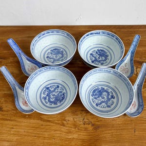 May include: Four blue and white porcelain bowls with dragon motifs and matching spoons. The bowls feature a delicate, perforated pattern and a central blue dragon design. The spoons have a blue and white floral pattern.